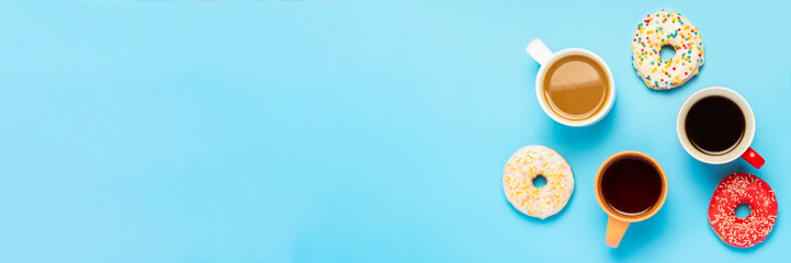 Tasty donuts and cups with hot drinks, coffee, cappuccino, tea on a blue background. Concept of sweets, bakery, pastries, coffee shop, meeting, friends, friendly team. Banner. Flat lay, top view