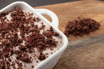 Tasty homemade pudding with chocolate crumble cookie in ceramic plate on wooden background.