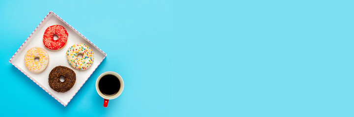 Tasty donuts in a box and a cup with hot coffee on a blue background. Concept of sweets, bakery,...