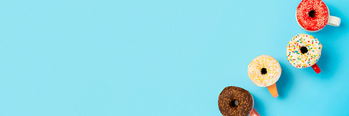 Tasty donuts and cups with hot drinks on a blue background. Concept of sweets, bakery, pastries, coffee shop. Banner. Flat lay, top view