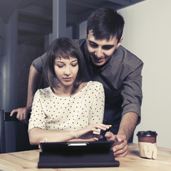 Happy young couple with tablet computer sitting at the table in apartment
