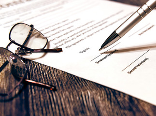 Fototapeta premium Contract sheet with glasses and pen on a wooden background