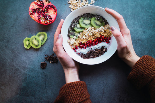 Healthy breakfast: Woman's hands holding a smoothie bowl with cereals and fruits. Flat lay.
