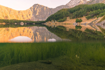 mirroring on a mountain lake and looking below the surface, high mountains in the background