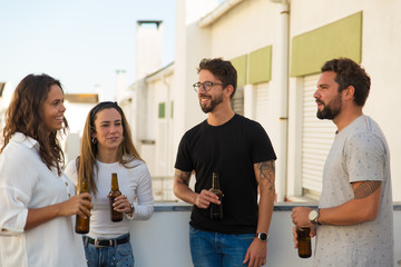 Smiling friends talking while drinking beer. Group of young people hanging out together. Communication concept