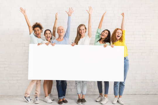 Group Of Women Holding Blank Poster Posing Near Wall Indoor