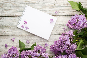 Clean notepad with spring lilac flowers on white wooden background