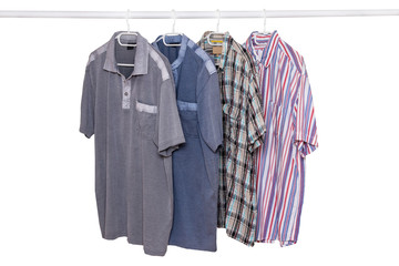 Hanging shirts isolated. Closeup of collection of four male various colorful t-shirts on a clothes rail isolated on a white background. Mens summer fashion.