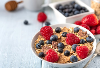 Healthy breakfast of granola chips with blueberries and raspberries on white desk.