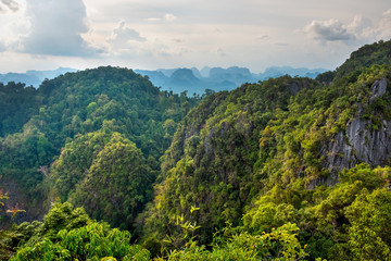 Mountain landscape with rainforest and cloudy sky bathed in sunlight. Far away in a haze a valley with hills is visible