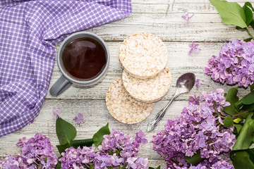 Cup of tea with crispbreads decorated spring lilac flowers on white wooden background