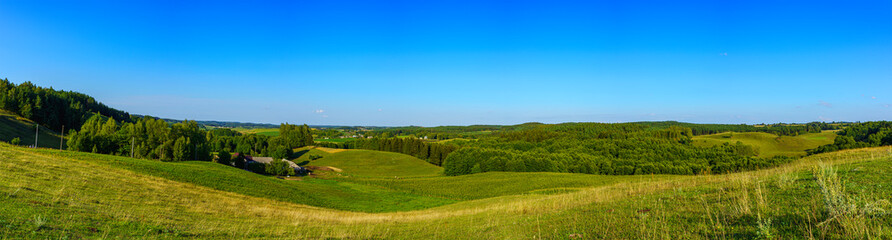 Panoramic view of the undulating landscape with meadow and trees in autumn colors, and ble sky.