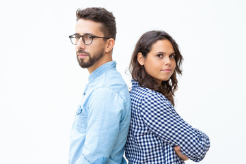 Confident man and woman standing back to back. Side view of serious young couple standing together and looking at camera on white background. Confidence concept