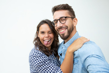 Obraz na płótnie Canvas Happy couple grimacing and looking at camera. Cheerful young man and woman fooling around in studio on white background. Friendship concept