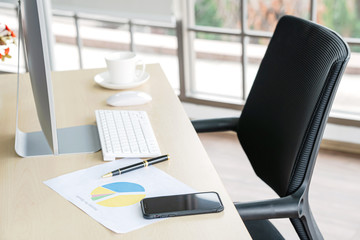 Business and workplace concept. Cup of hot coffee on work desk with computer keyboard Mobile and papers graphs in office working room.