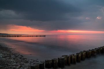 Long time exposure of colorful sunset at a beach of the baltic sea with groins in the forground