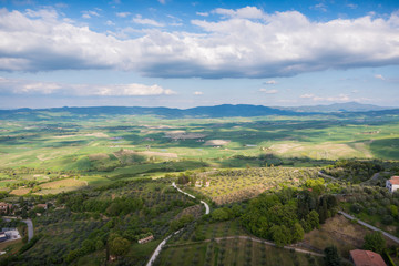 Beautiful landscape in Val d'Orcia in Tuscany in Italy with green and yellow grass fields and trees with sky with clouds and typical tuscany trees cypresses and sweet hills at sunrise