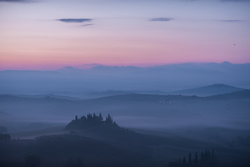 Podere belvedere house on a hills in tuscany in italy at sunrise with beautiful light and myst and fog on sweet hills with cypresses trees