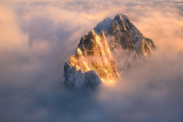 The top of the mountain runs out of the inverse cloud and is illuminated by the rising sun.