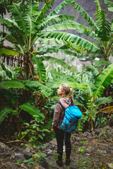 Blond young women with blue backpack admire banana plantation on the trekking route to paul valley on santo antao island, cape verde
