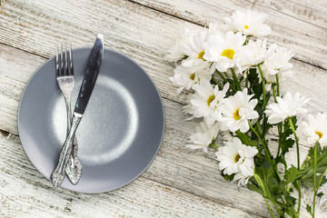 empty plate with fork and knife decorated with chamomile flowers on white wooden background