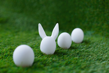 White chicken eggs on green grass, behind which are hidden the ears of the Easter bunny, which are symbols for the celebration of religious holiday among Christians and Catholics