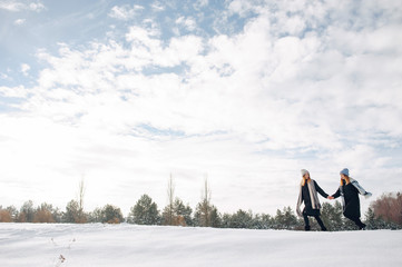 Cute girls walking in a winter park. Sisters have fun with snow. Ladies in a cute hats