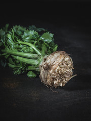 Celery root with green leaves on dark background.