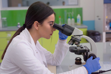 Young female scientist looking through a microscope in a laboratory doing research, microbiological analysis, medicine.