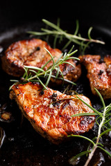 Fried pork tenderloin divided into portions with the addition of herbs and spices in the pan, close-up
