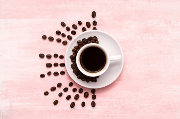 Cup of black coffee with a white saucer and coffee beans on a colored pink wooden background. Creative feed. Top view. Flat lay