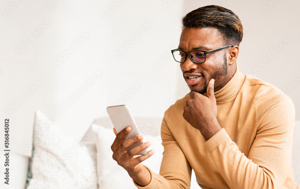 Poster afro man using cellphone texting sitting on sofa at home