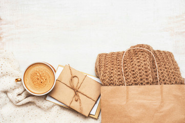 Coffee cup, packet with beige brown knitted scarf and correspondence, letters on vintage white wooden background with space. Top view. Flat lay