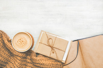 Obraz na płótnie Canvas Coffee cup with beige brown knitted scarf and correspondence notebook on vintage white wooden background with space. Top view. Flat lay