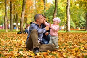 Fototapeta premium Mom, dad and daughter are playing on autumn leaves