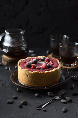Nordic dessert. Homemade lingonberry pie topped with wild berries and rosemary served with black coffee on black background copy space. Low key still life with natural lighting