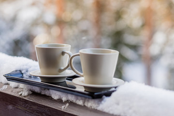 Steaming hot coffee in two mugs, buried in snow, on a balcony, on a bright winter morning. Breakfast for two. Cozy winter concept.Morning chill out on the fresh air,cup of tasty coffee.Winter still