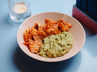 Nachos with guacamole in the plate on blue table