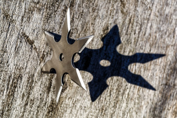 Shuriken (throwing star), traditional japanese ninja cold weapon stuck in wooden background,Silver shuriken with star shape.Samurai, throwing weapons © bukhta79
