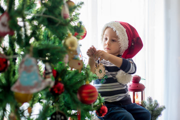 Beautiful blonde toddler boy, decorating christmas tree with balls and light strings