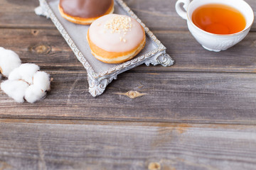 Donuts made of white milk chocolate, coated with glaze and nuts. Aristocratic tea party with porcelain cup on a wooden table background. Decorated with vases, cotton inflorescences, white sugar bowl