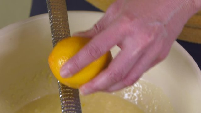 Closeup of baker zesting lemon zest using grater over mixing bowl adding to delicious cake batter