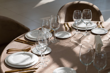 Chic and elegant, gold-plated cutlery and white plates, table setting with empty plates. Glasses in the light from the window.