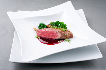 Fried dry aged venison tenderloin fillet medallion steak natural with kalette and raspberry sauce as closeup on a modern design plate