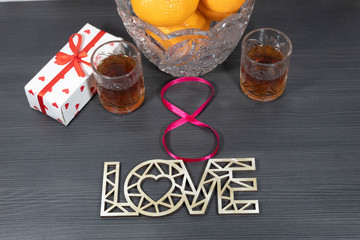 On the table there is a vase with tangerines, two glasses with alcohol, a gift box. Number 8 is laid out from a red ribbon and the word 