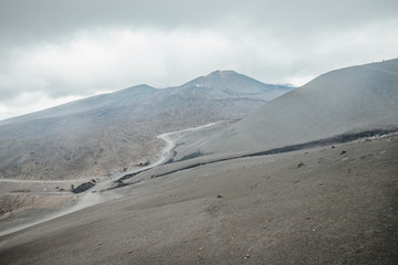 Top of crater Mount Etna volcano, frozen cold lava smokes, thick clouds