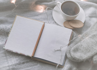 Cozy winter still life: mug of hot tea and book with warm plaid on windowsill against snow landscape from outside.