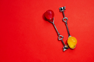 Two stylish metal silver teaspoons with hearts and round candies on a contrasting red background with copy space, top view. Valentine's Day concept.