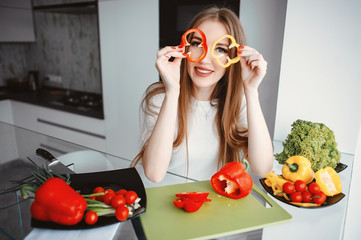 Woman in a kitchen. Blonde in a white t-shirt. Woman with vegetables