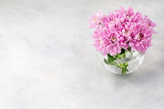 Pink flowers in a glass vase with on a light grey table. Background for Valentine Day, Mothers Day or Birthday. Space for text.